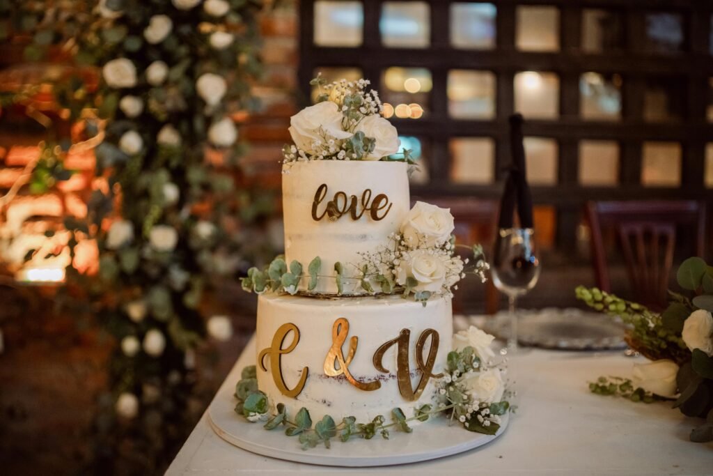 Charming two-tier wedding cake adorned with white roses and eucalyptus leaves in elegant indoor setting.